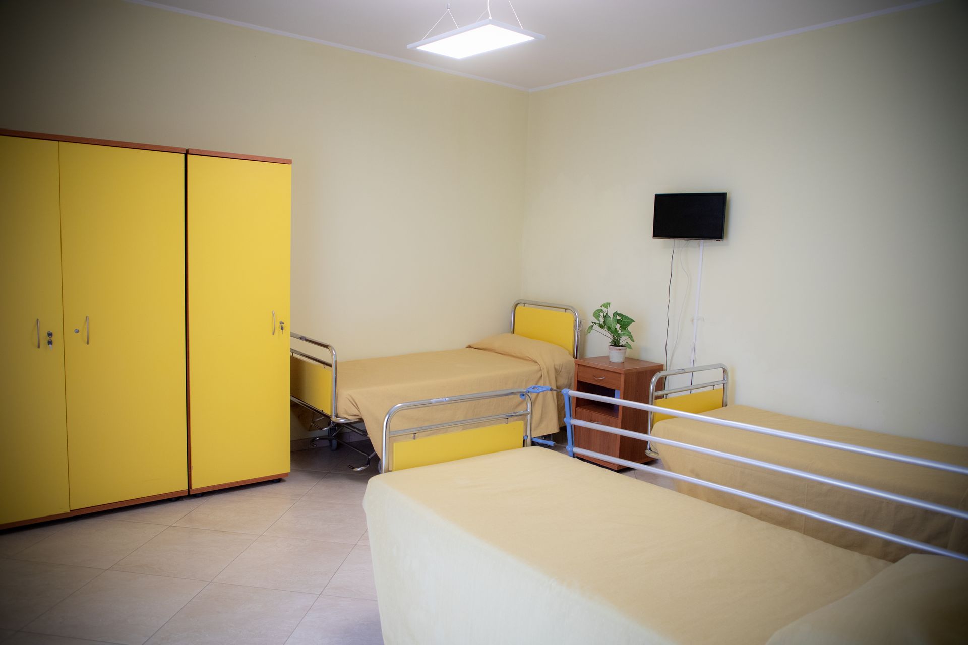 Due letti in una stanza semplice con armadio giallo, pareti beige e una piccola TV.