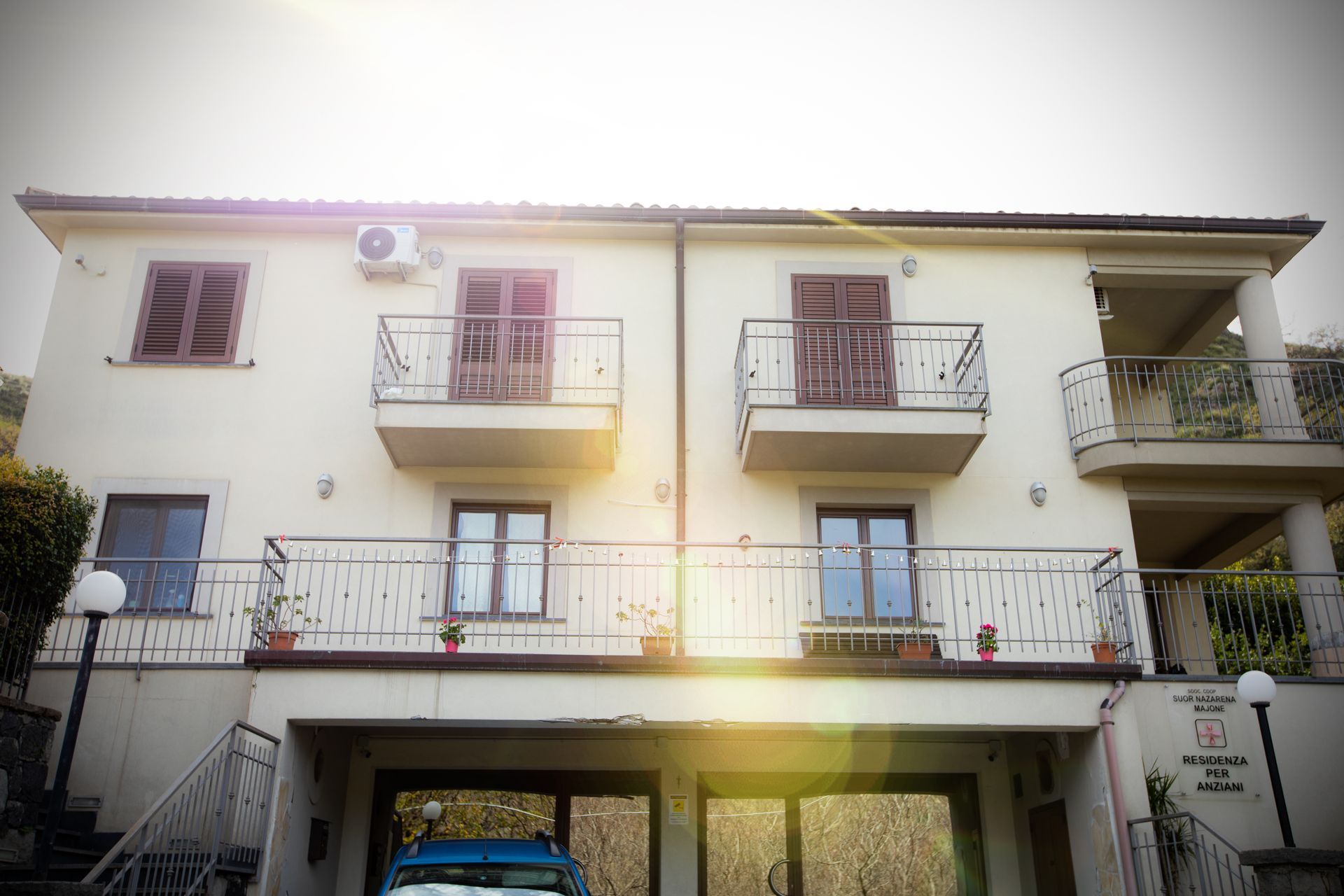 Edificio color crema a due piani con balconi e persiane marroni. Un'auto è parcheggiata in garage.