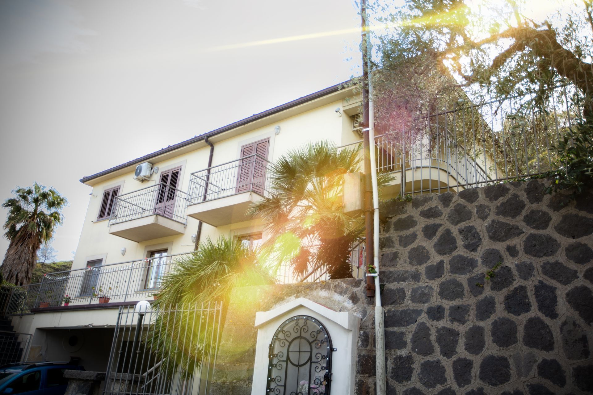 Un edificio giallo chiaro a due piani con balconi, ringhiere in ferro battuto e un muro di pietra. 