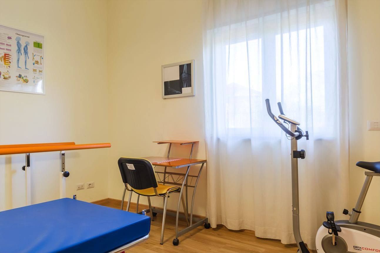 Sala di fisioterapia con attrezzi ginnici, scrivania e finestra.
