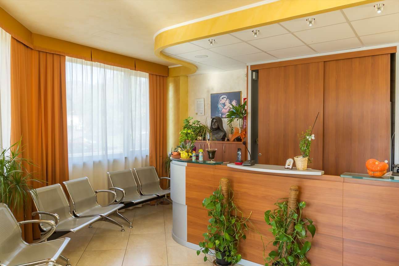 Area reception con scrivania in legno marrone, sedie e piante in vaso.