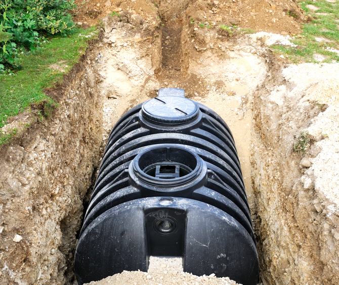 Black septic tank installed in a dug trench in a yard, visible top opening and access hatch.