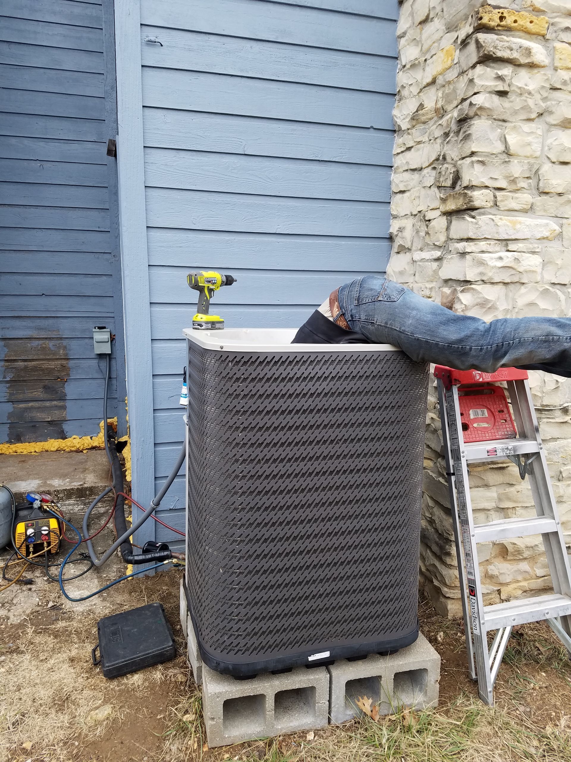 A man laying on a ladder next to an air conditioner