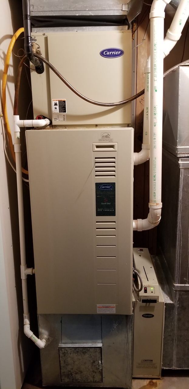 A carrier air conditioner is sitting in a basement next to a washer and dryer.
