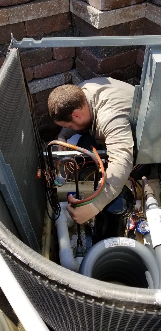 A man is working on an air conditioner in a hole in the ground.
