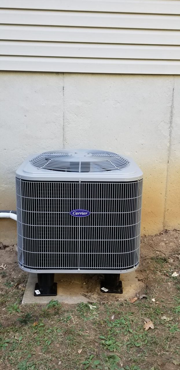 A carrier air conditioner is sitting outside of a house.