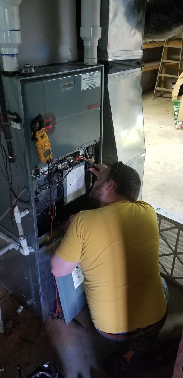 A man in a yellow shirt is working on an air conditioner.
