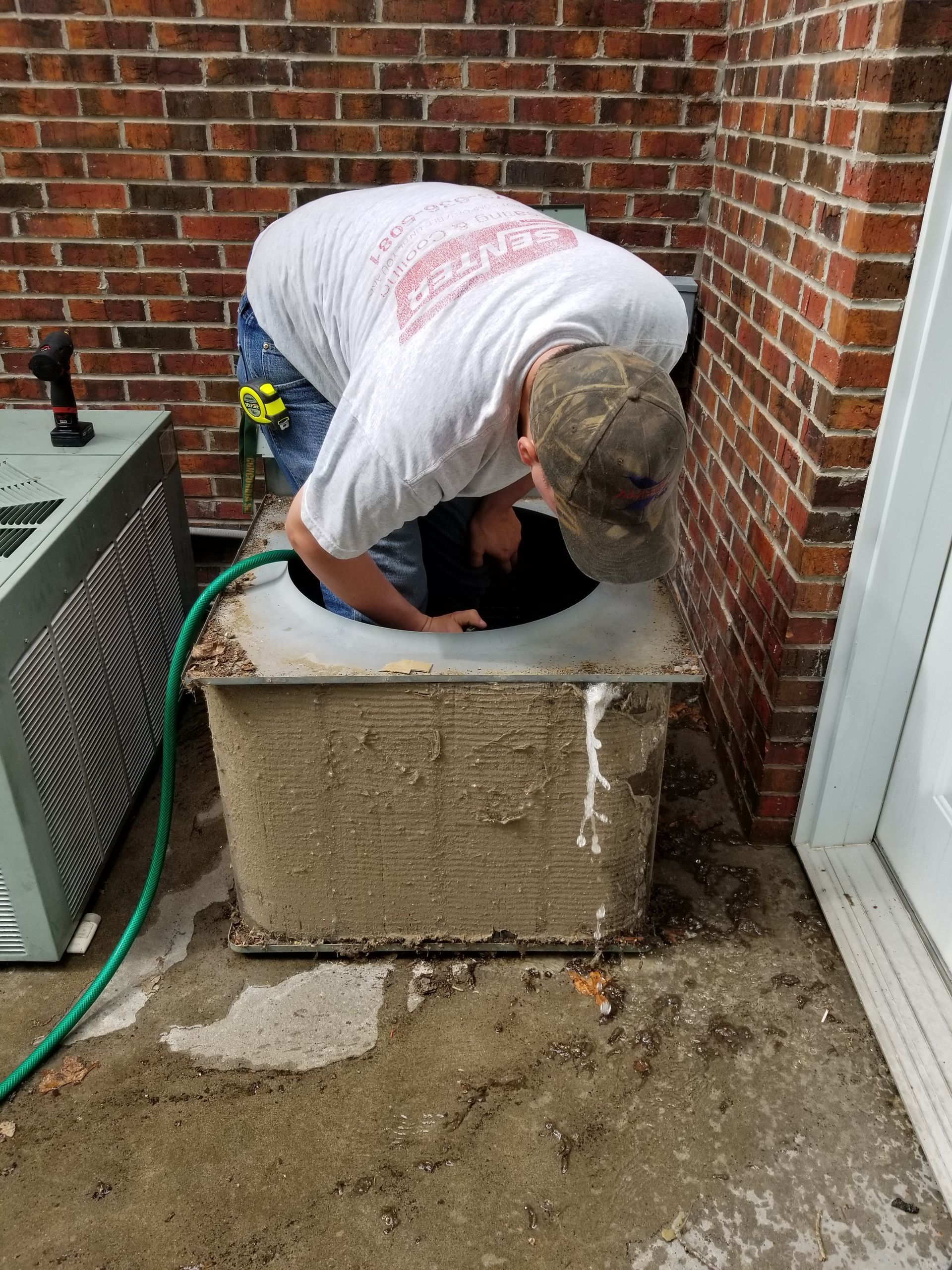 A man is working on an air conditioner outside of a brick building