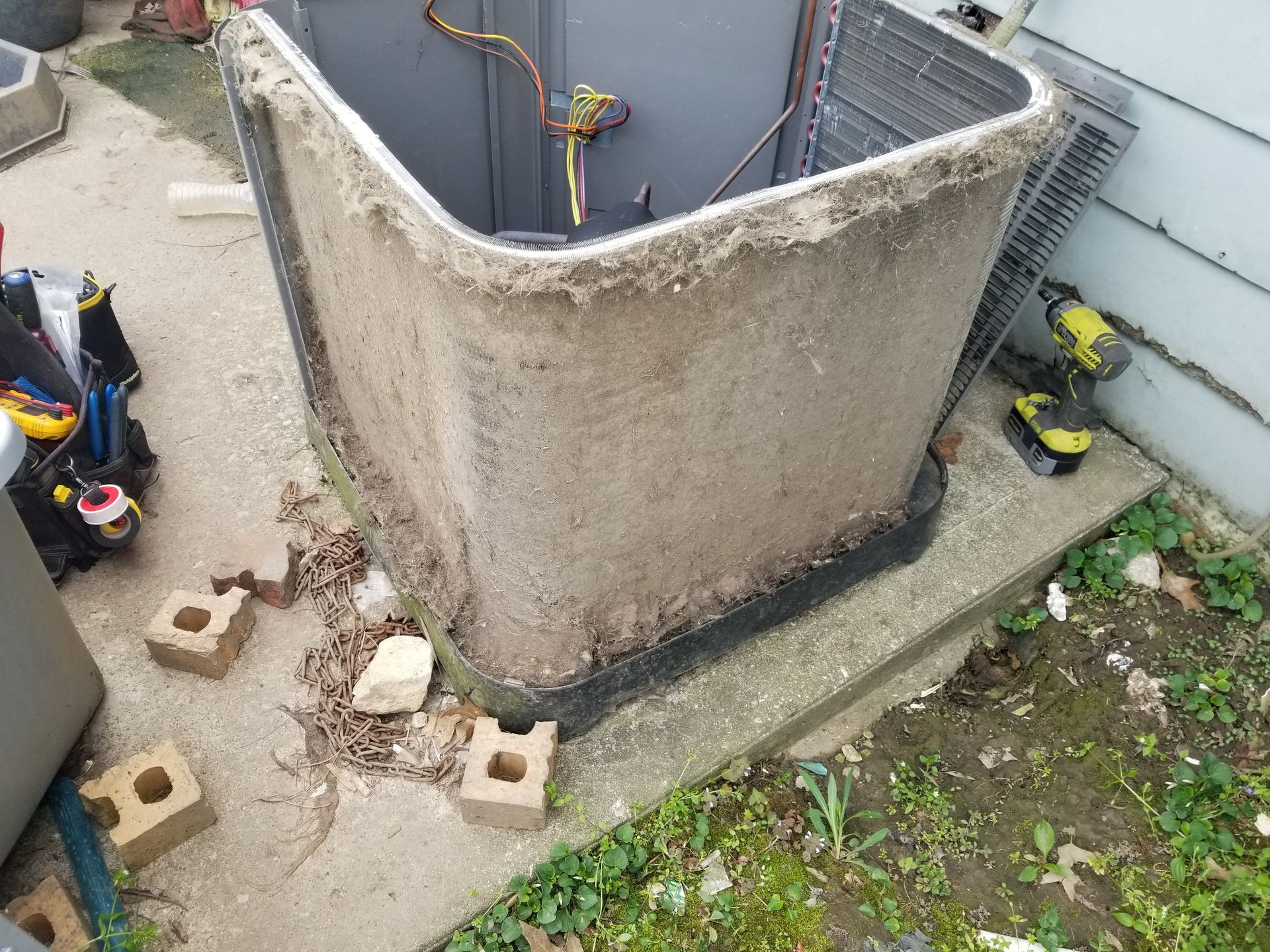 A dirty air conditioner is sitting on the ground next to a toolbox.