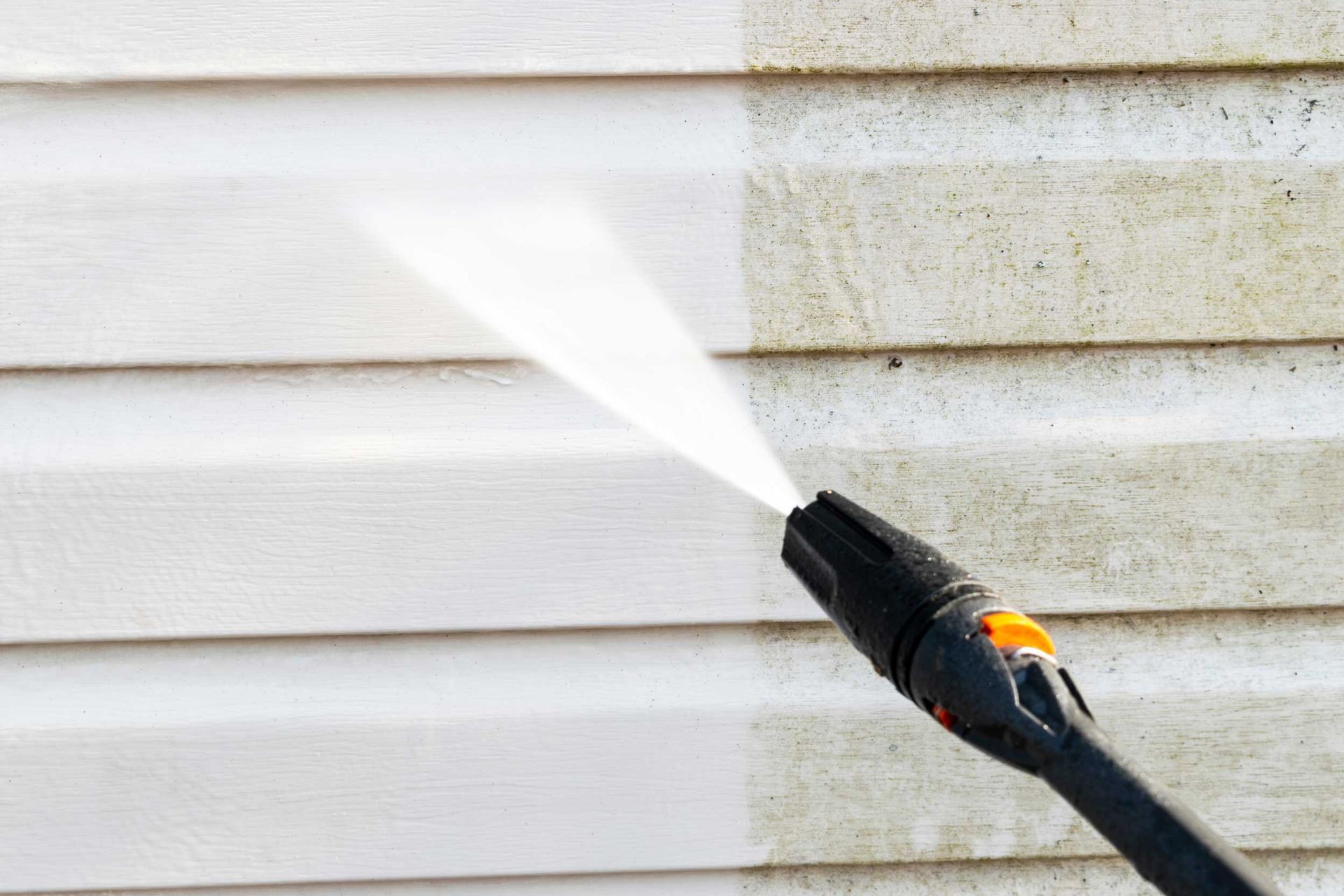 Pressure washing services removing mold and dirt from white vinyl house siding exterior wall.