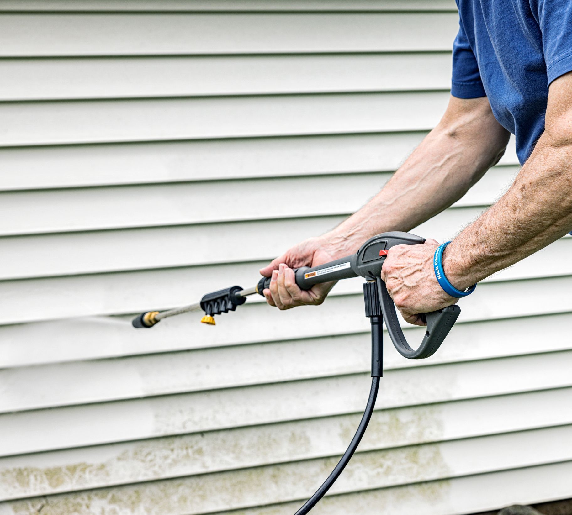 Senior man doing power washing siding to a house.