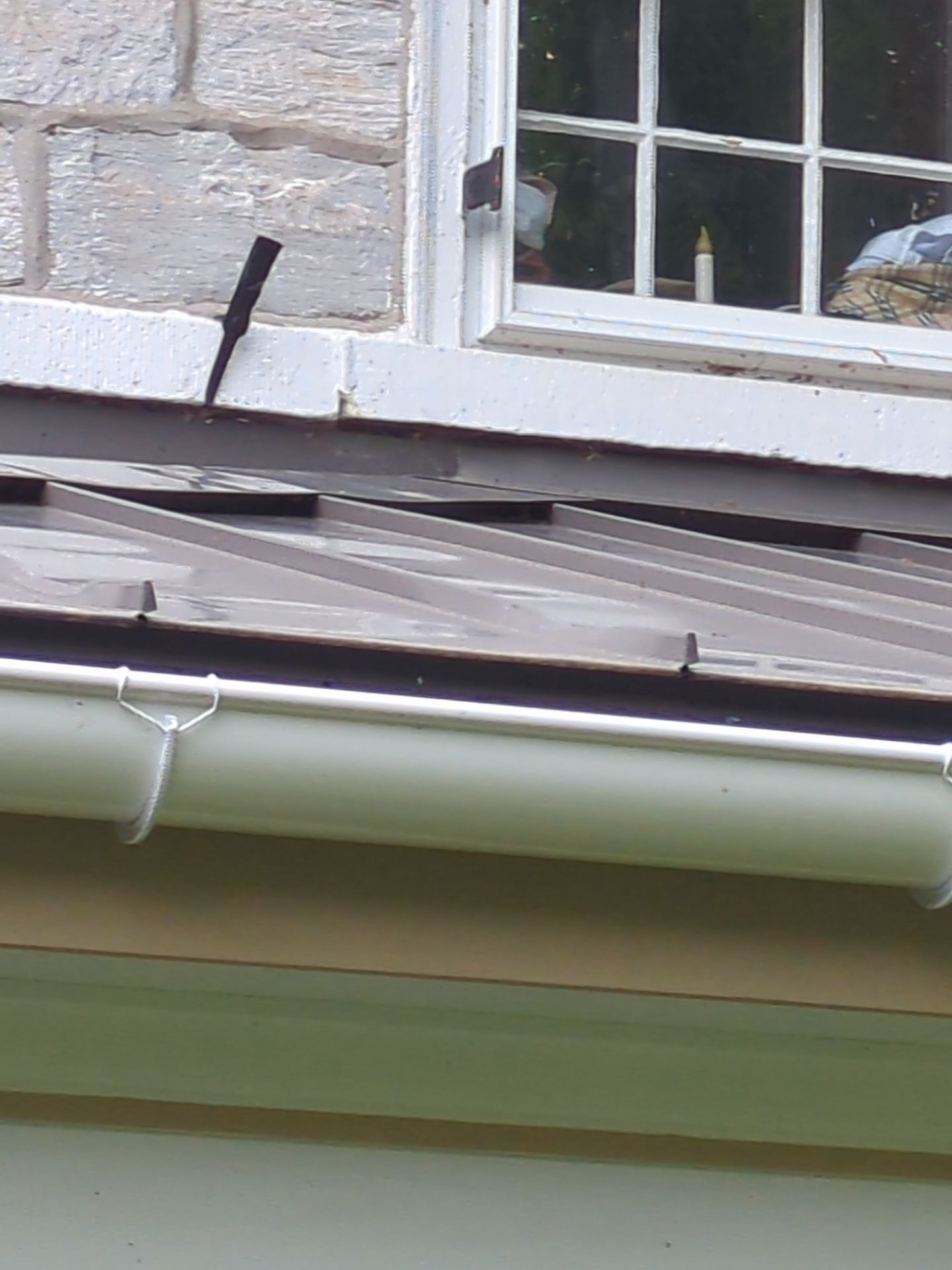 Brown metal roof with a white-framed window above, and a light green gutter.