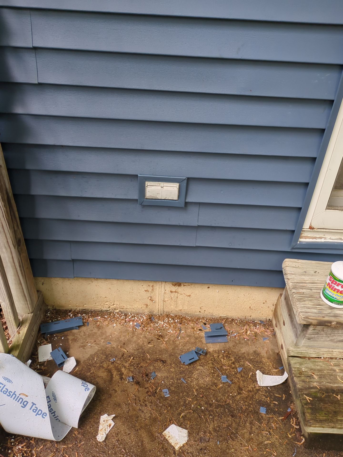 Blue siding with vent, debris on the ground, and a small porch.