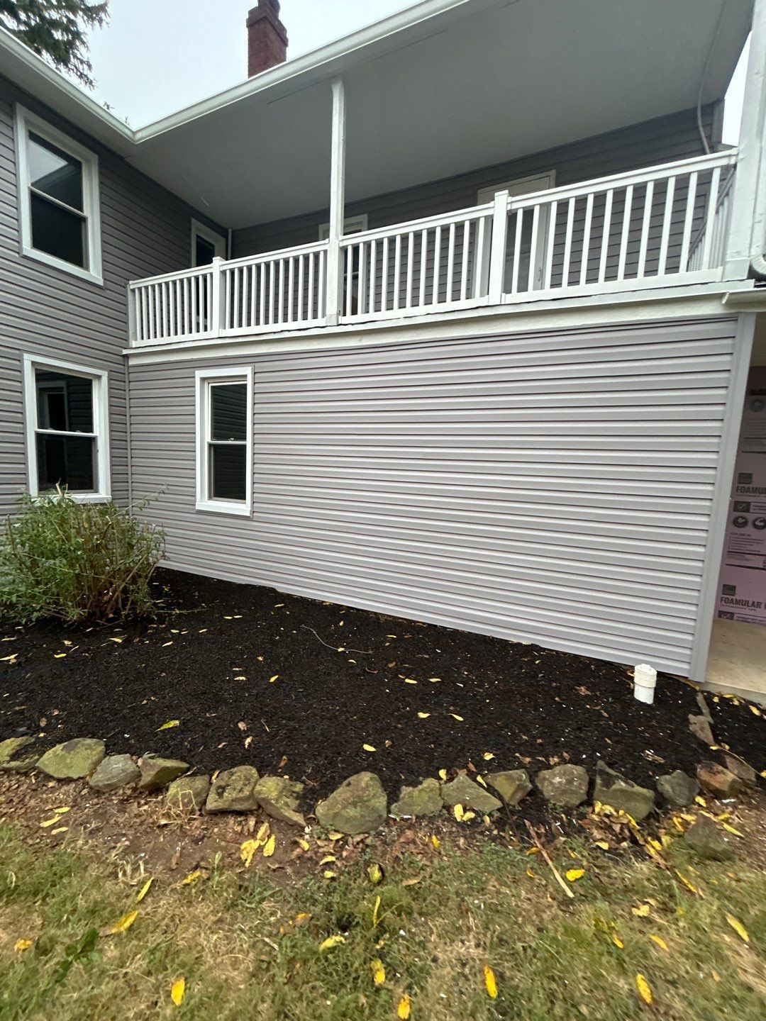 Gray house with a porch and white railing, gray siding, and a dark mulch bed.