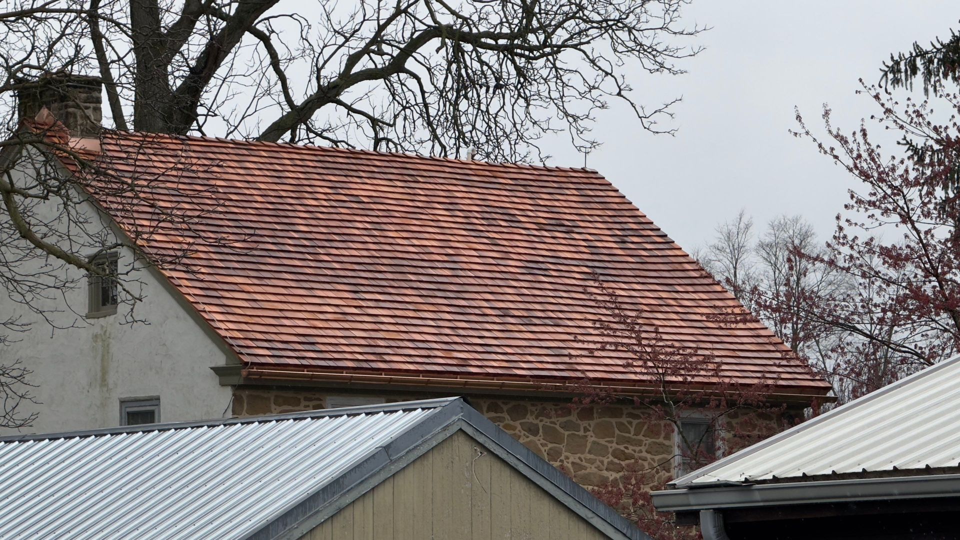 Large beige house with a turret and dark roof, under a cloudy blue sky. A car is in the driveway.