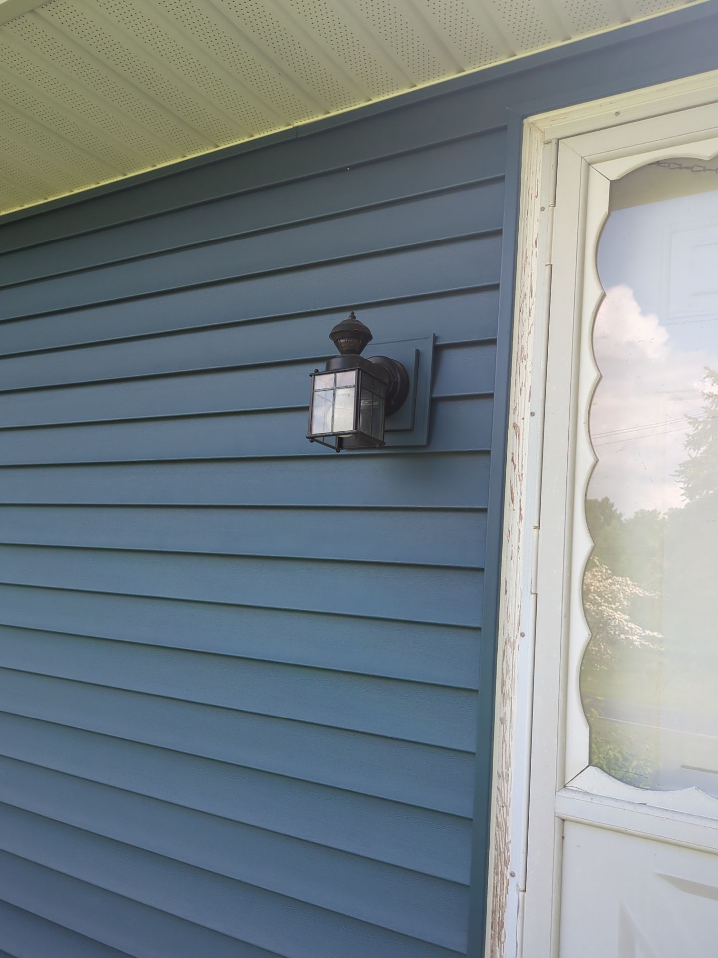 Blue siding on a house with an outdoor light fixture mounted on the wall.