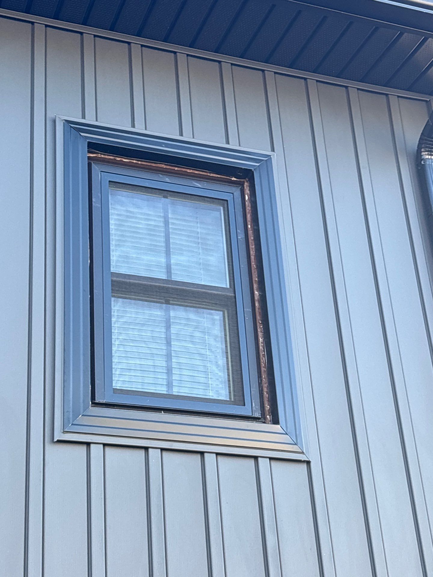 Window with blue trim on a light gray corrugated metal wall.
