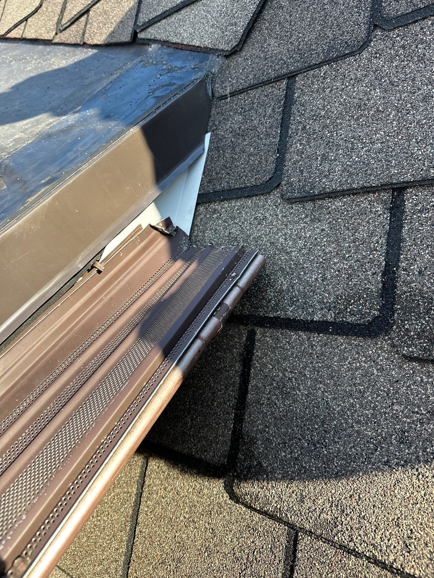 Brown gutter and roof flashing meet asphalt shingles.