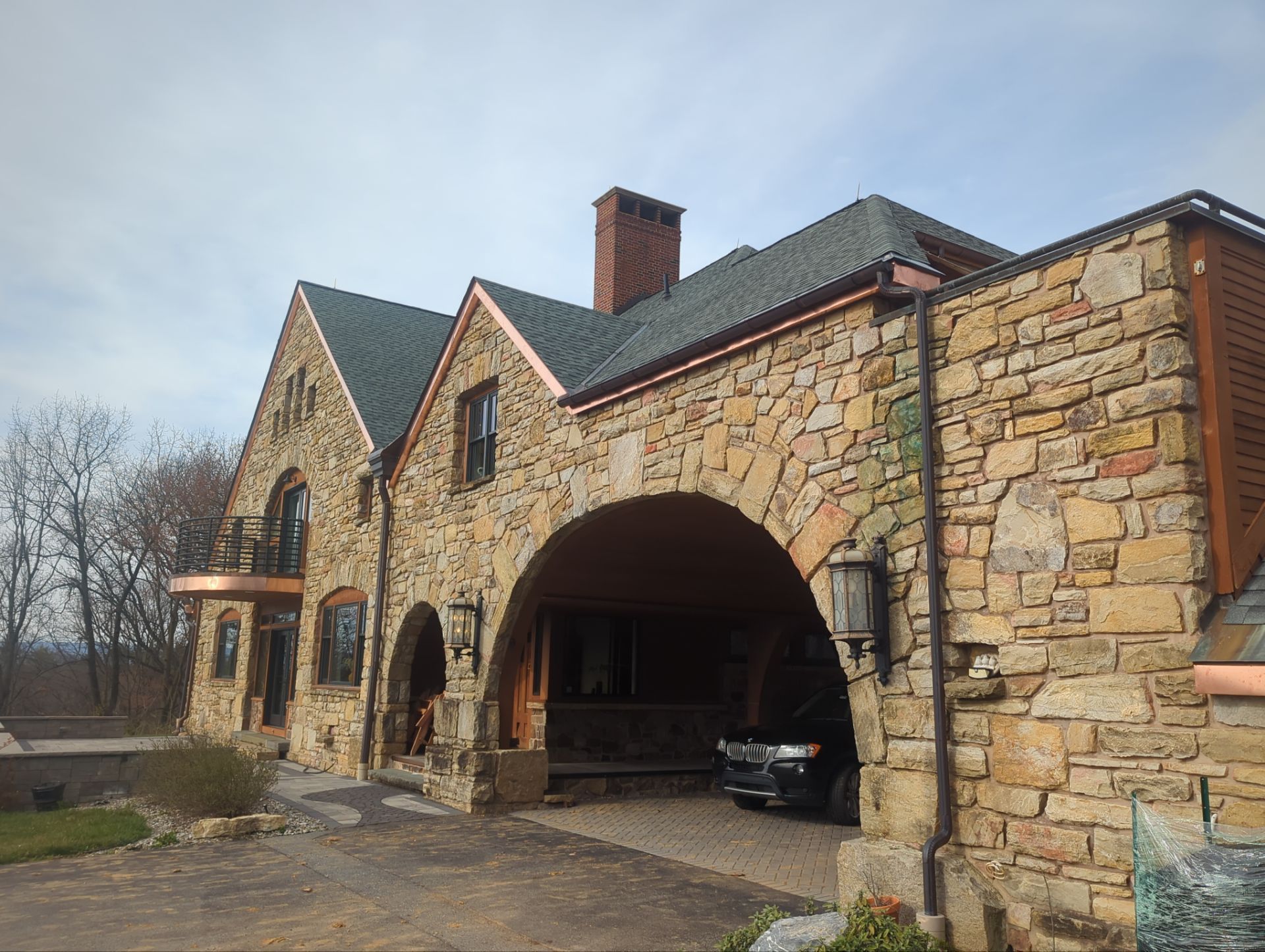 Stone house with archway over driveway. Copper gutters and green shingle roof.
