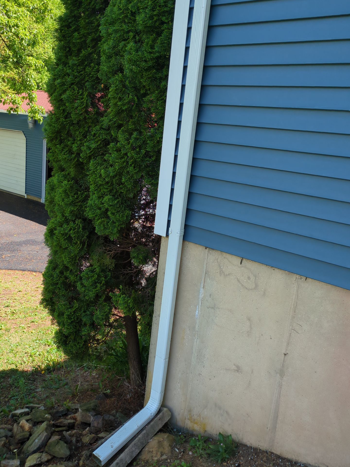 White gutter along blue siding and beige foundation next to a green tree.