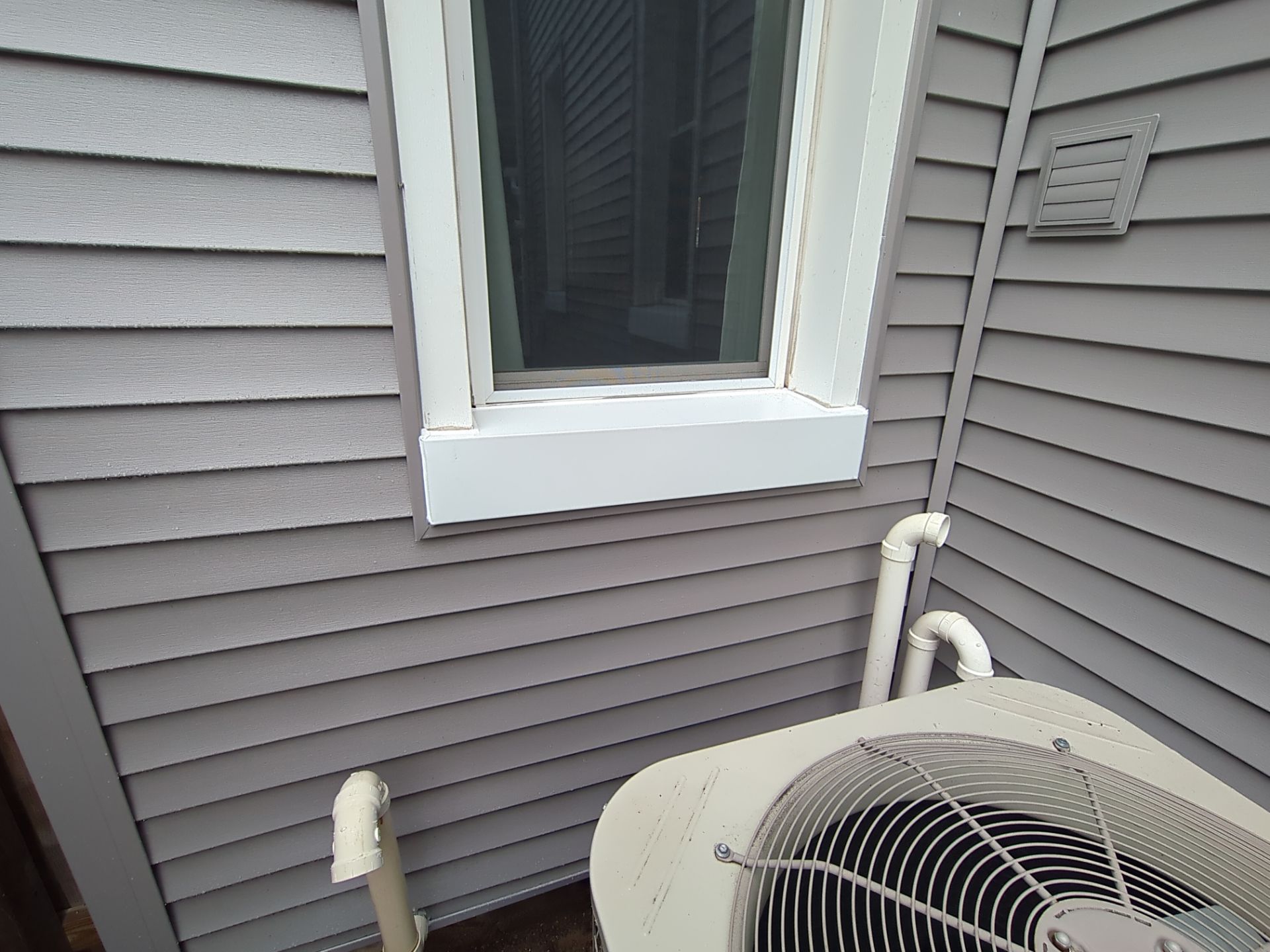 Gray house siding with a white-framed window. An air conditioning unit sits below.
