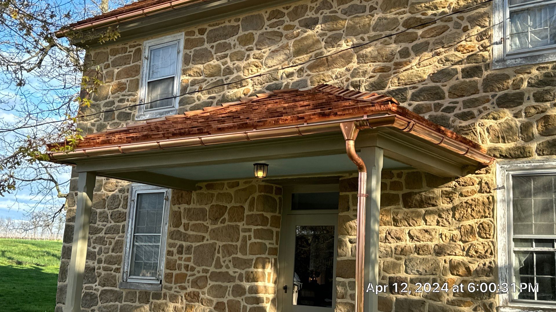 Stone house with porch. Copper-colored roof, and gutters. Light-colored stone walls. Blue painted ceiling on porch.