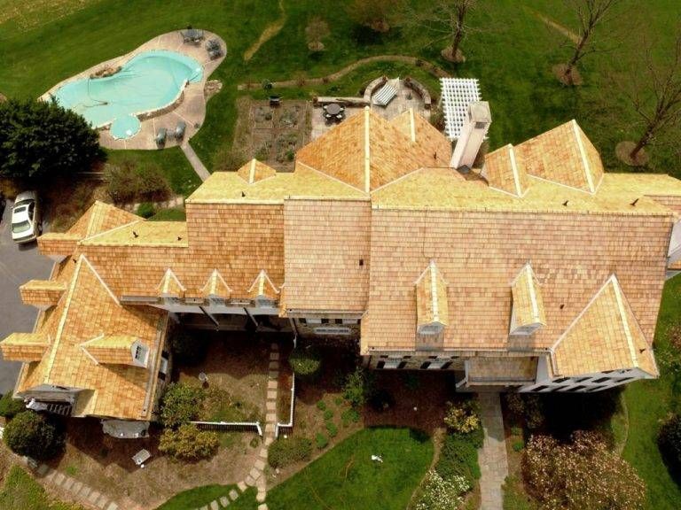 Aerial view of a large house with a cedar shake roof and a pool in the backyard.