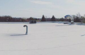 Flat white rooftop with metal vents and HVAC units under a blue sky. Trees in the background.