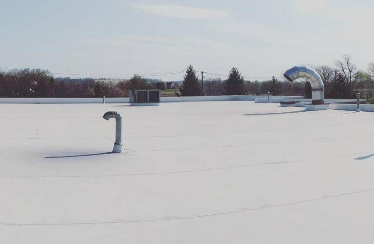 White rooftop with vents and pipes, under a sunny, light blue sky.