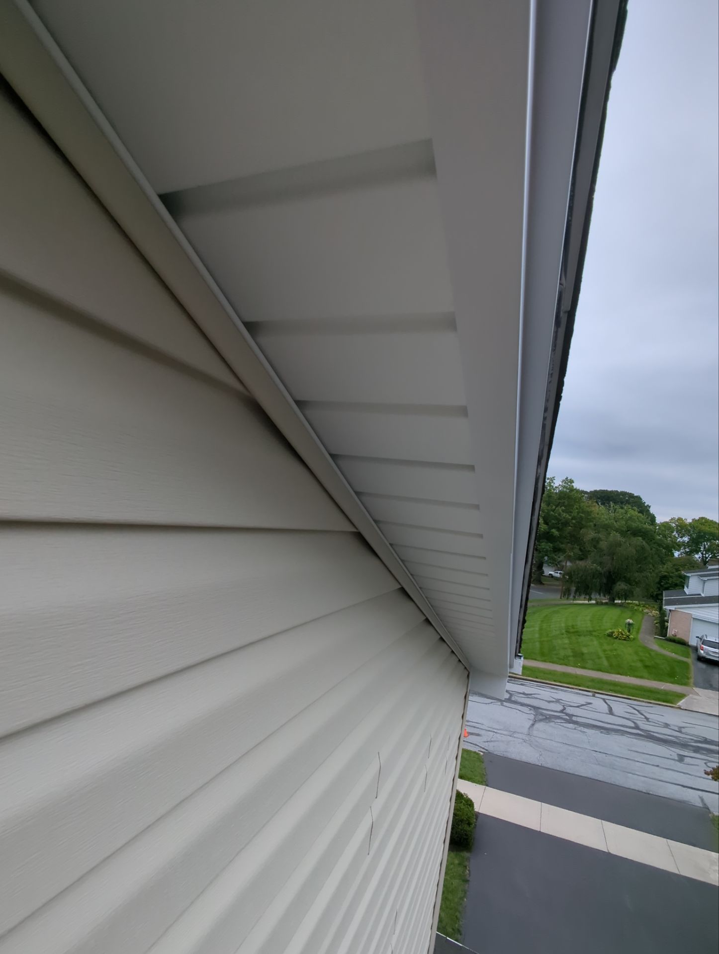White siding and soffit on a building's corner under a gray sky.