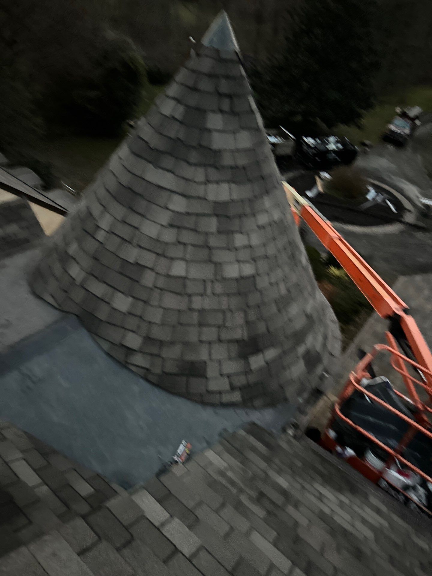 Conical roof with gray shingles, viewed from above, with an orange lift extending towards it.