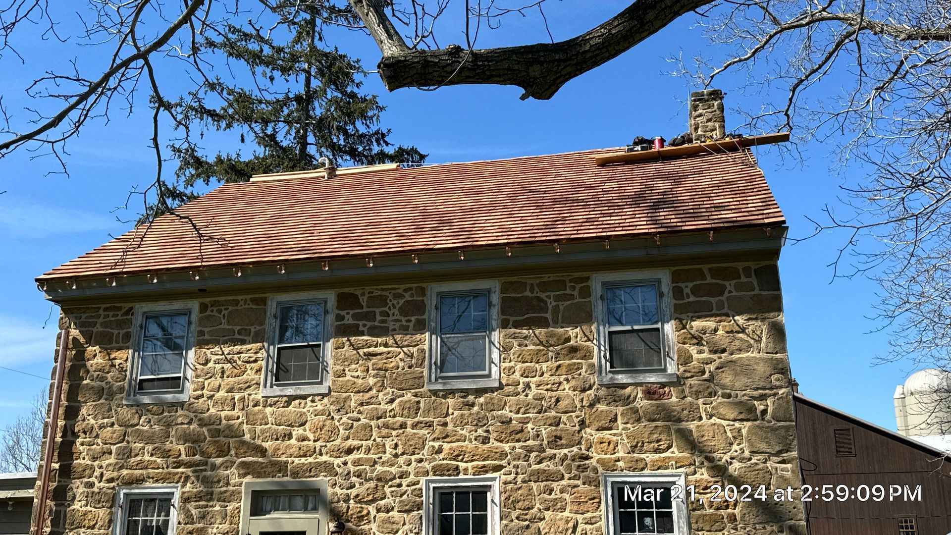 Stone house with wavy terracotta roof under a clear blue sky.
