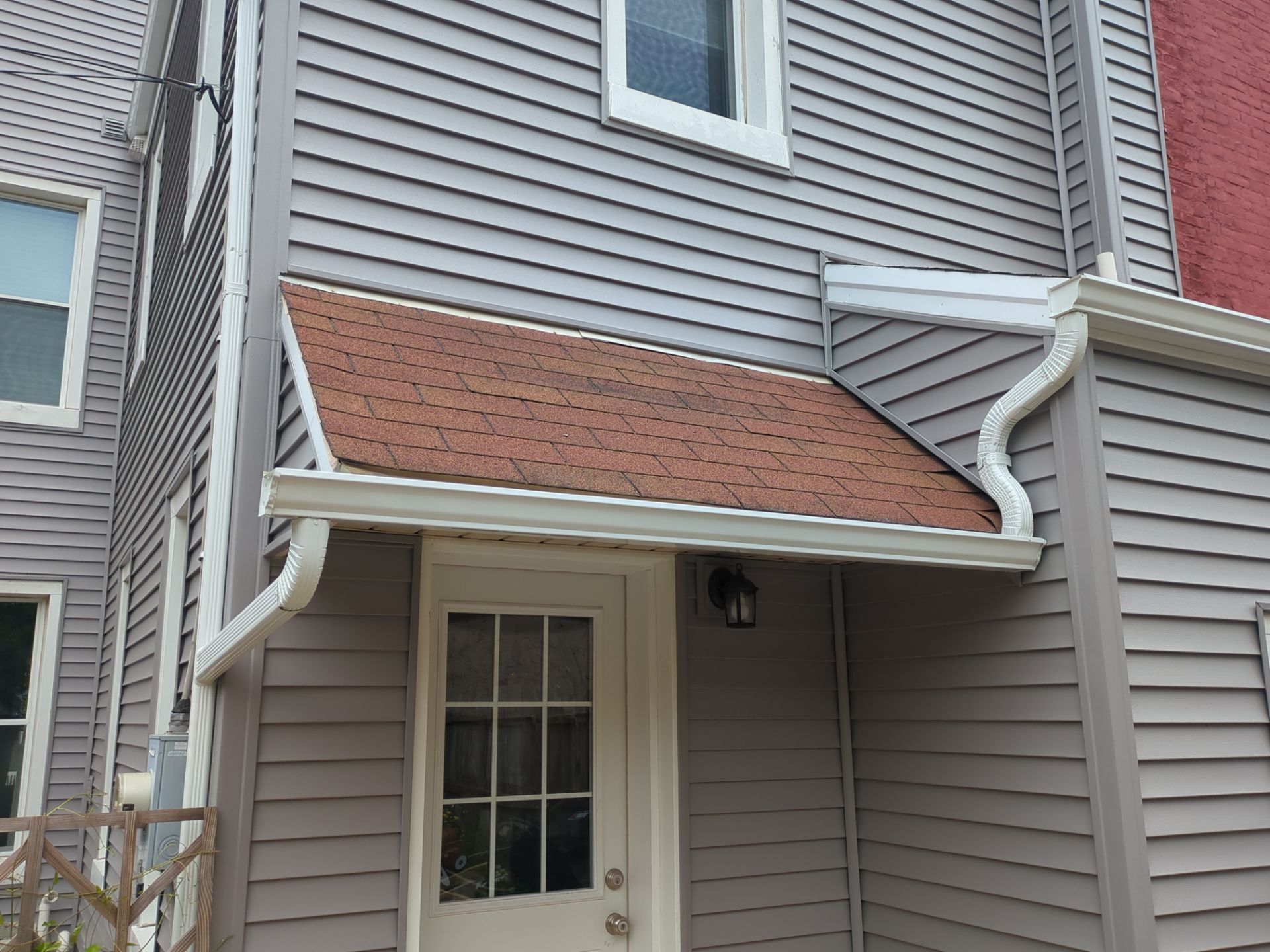Exterior of building with gray siding, small roof, white door, and gutters.
