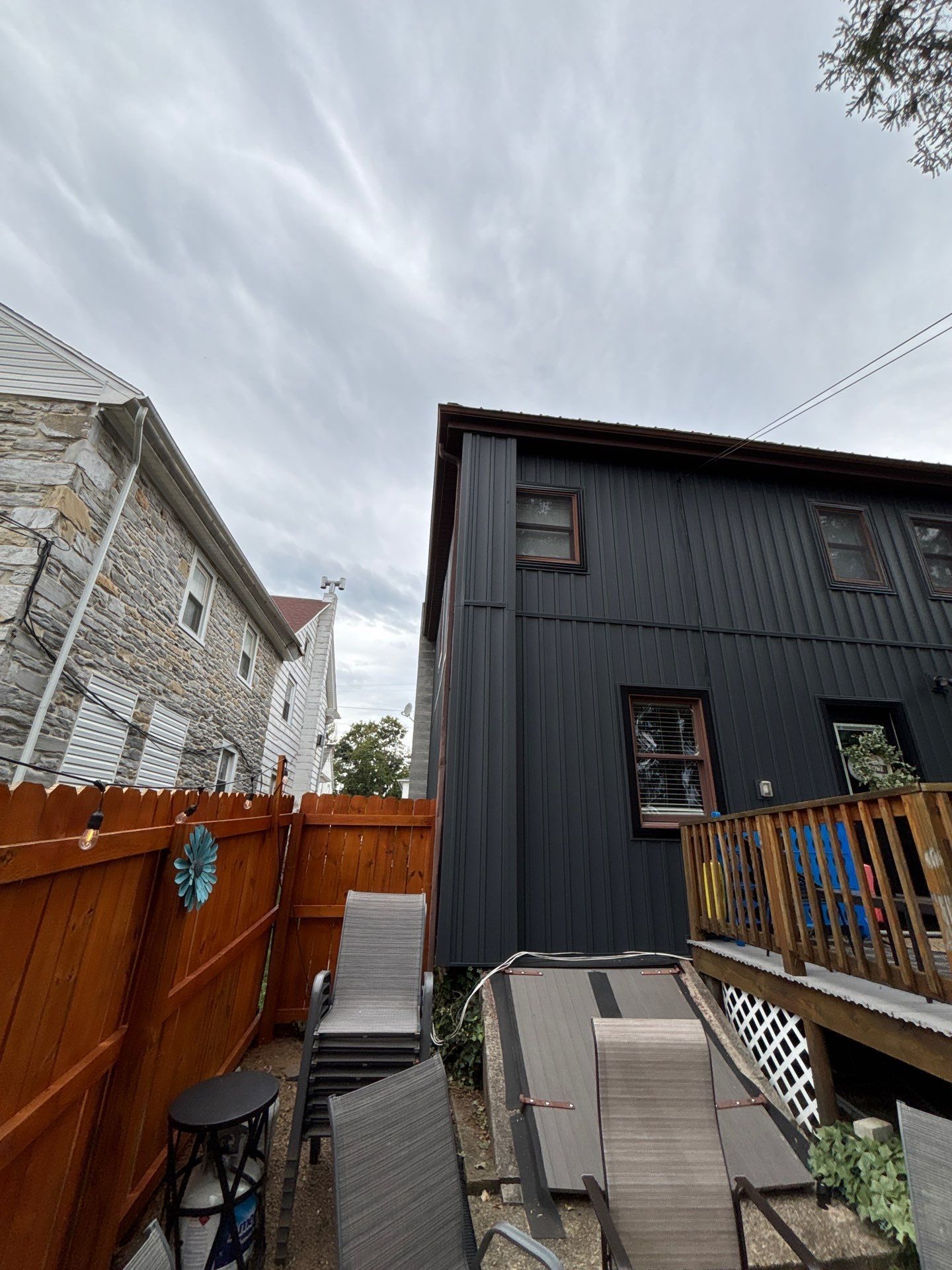 Backyard with black building, wooden deck, brown fence, and gray cloudy sky.