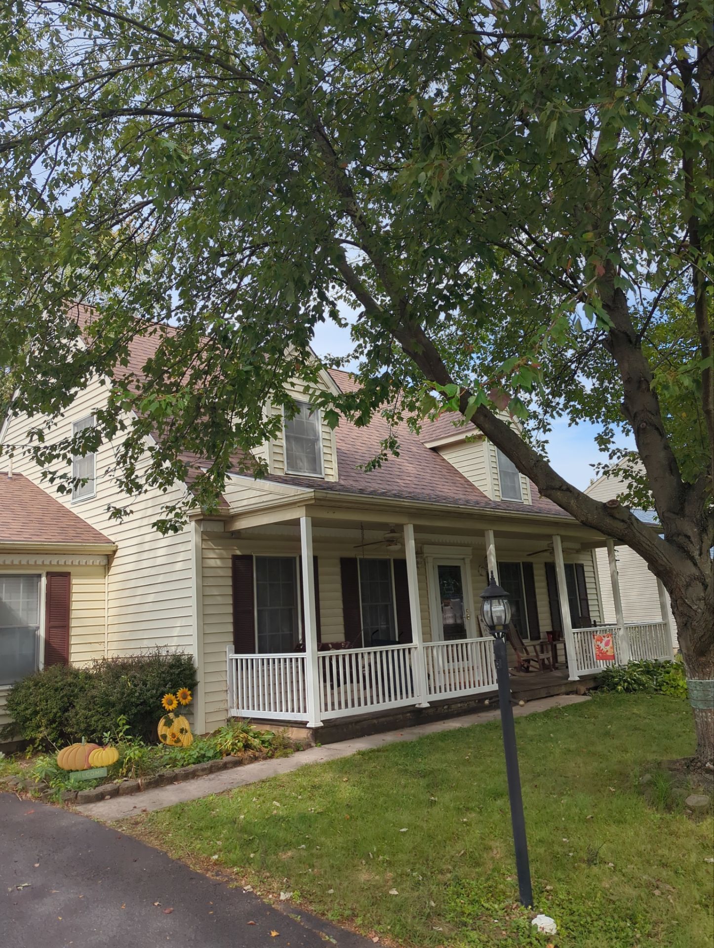 Brown shingle roof of a house against a blue sky with clouds, surrounded by trees.