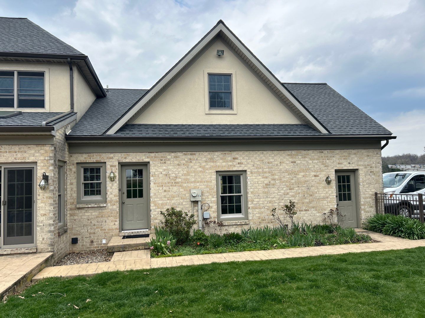 Tan brick house with gray roof and green grass in the yard.