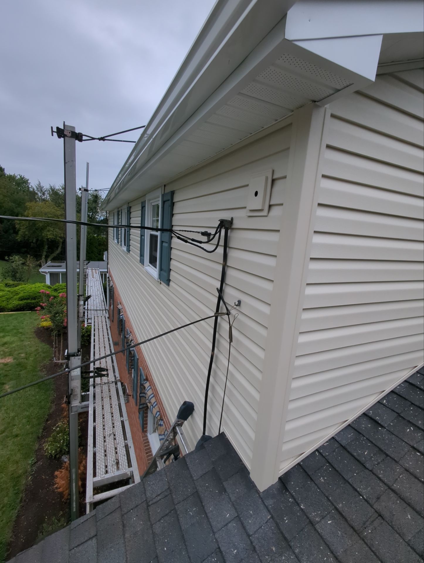 Beige vinyl-sided house with black electrical cables. Roof in foreground, utility pole to the left.