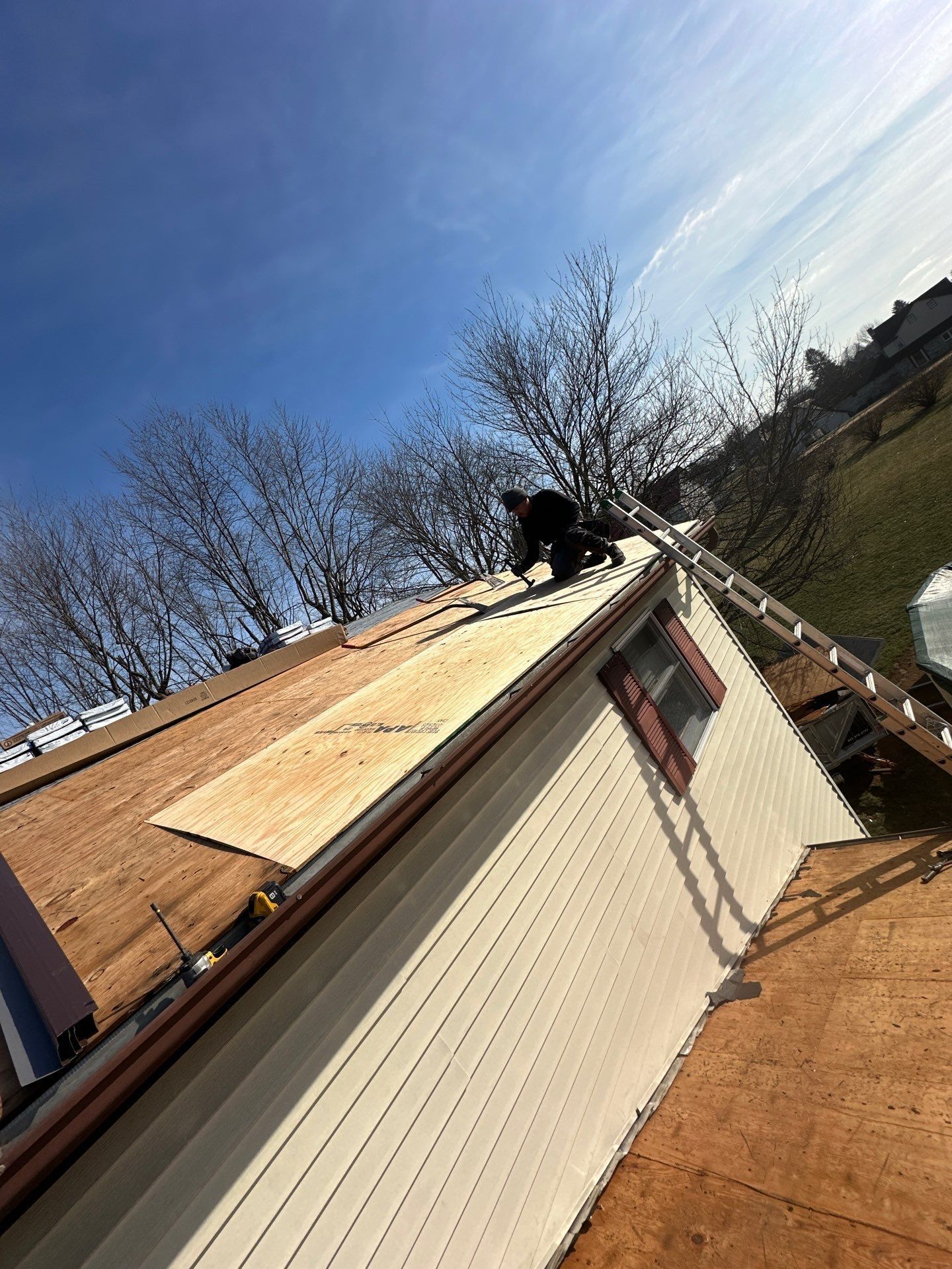 Person working on a roof, installing new wood panels. Sunny day, blue sky.