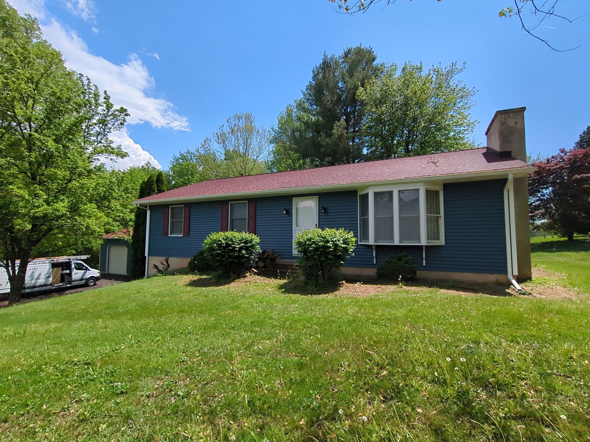 Stone house with arched entryway, balcony, and garage; trees in background.