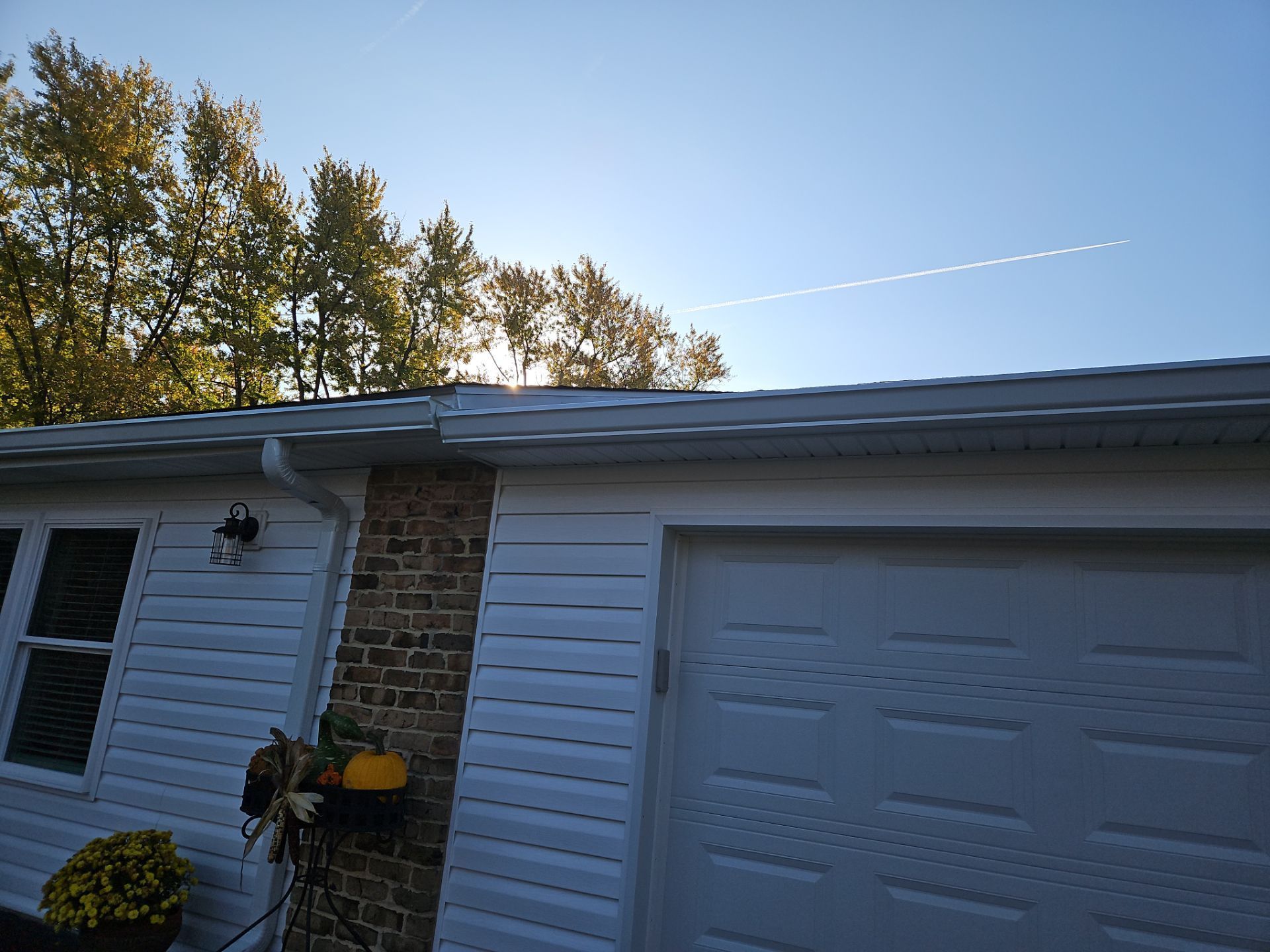 White garage and house exterior with trees in the background, contrail in the sky.