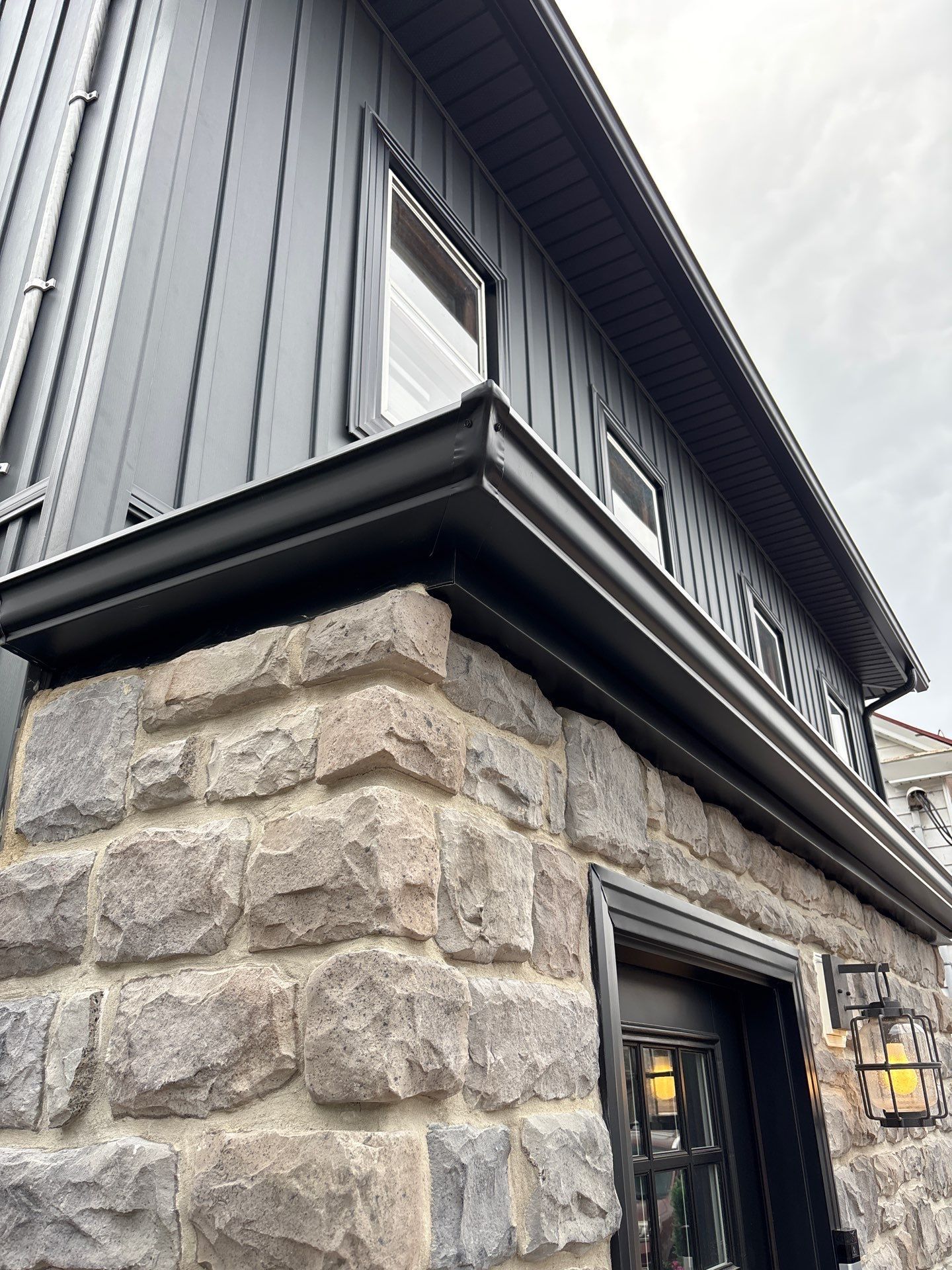 Stone building exterior with black trim, siding, and gutters; windows.