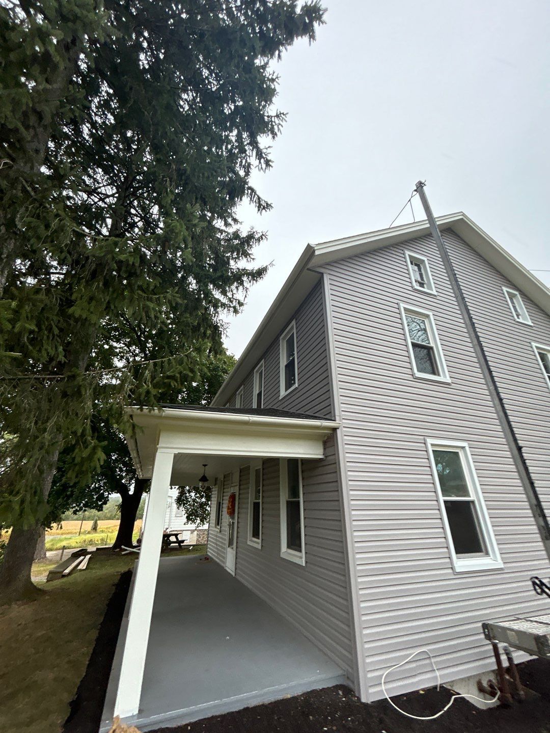 Gray house with white trim, long porch, and a tall tree on a cloudy day.