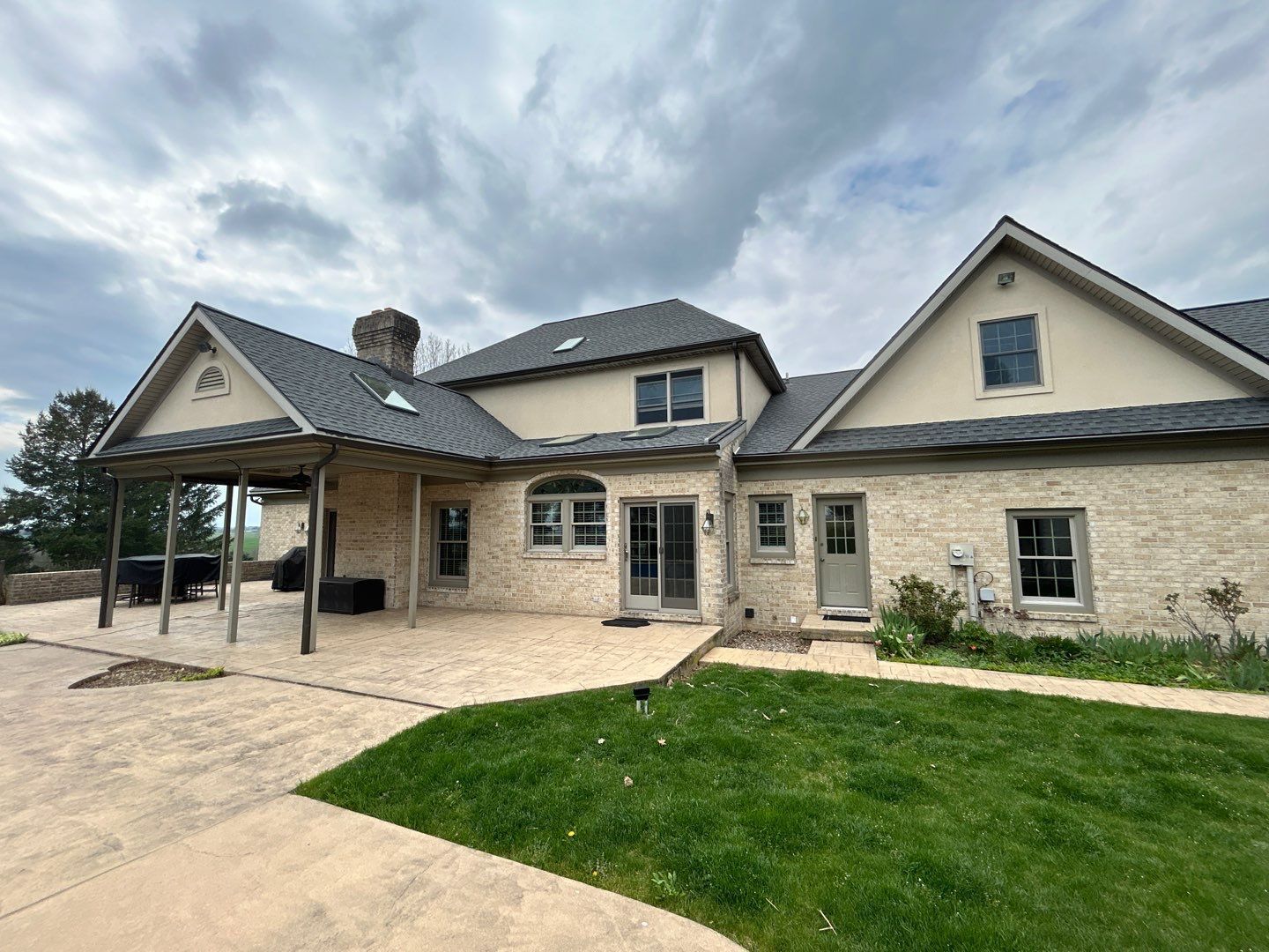 Back view of a light-colored brick house with a dark gray roof under a cloudy sky.