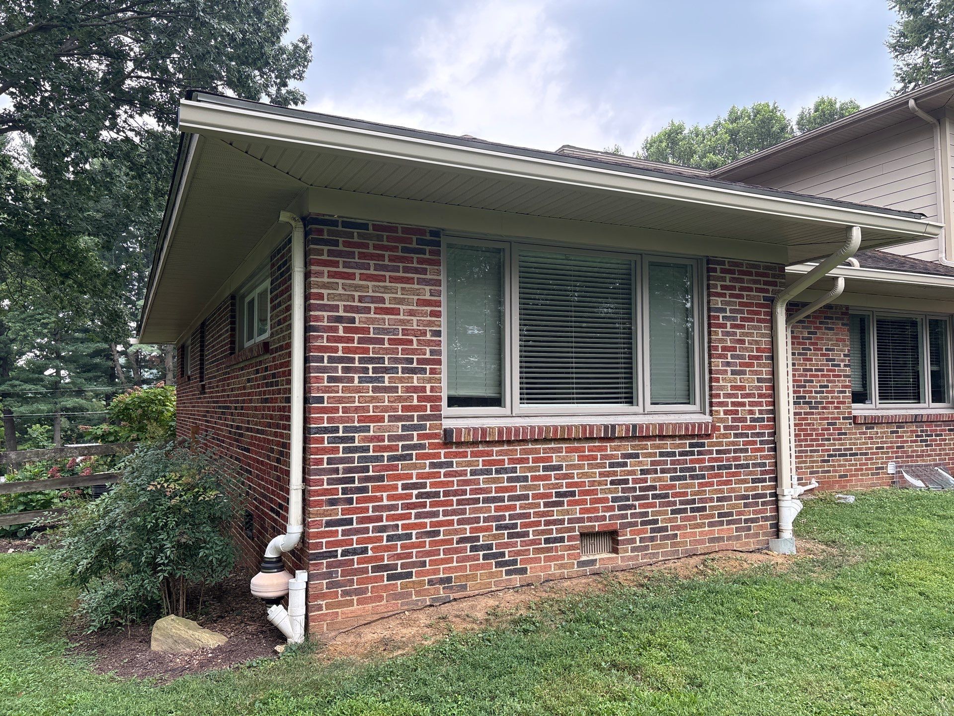 Red brick building with beige trim, gutters, and windows on a grassy lawn.