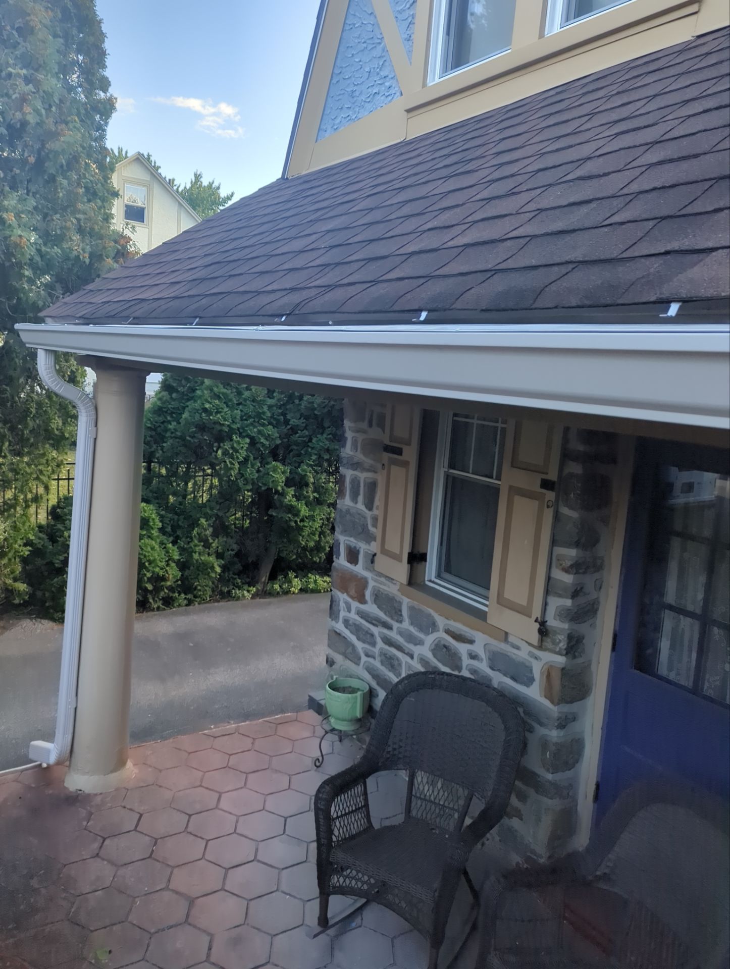 Stone house with arched entryway, balcony, and garage; trees in background.