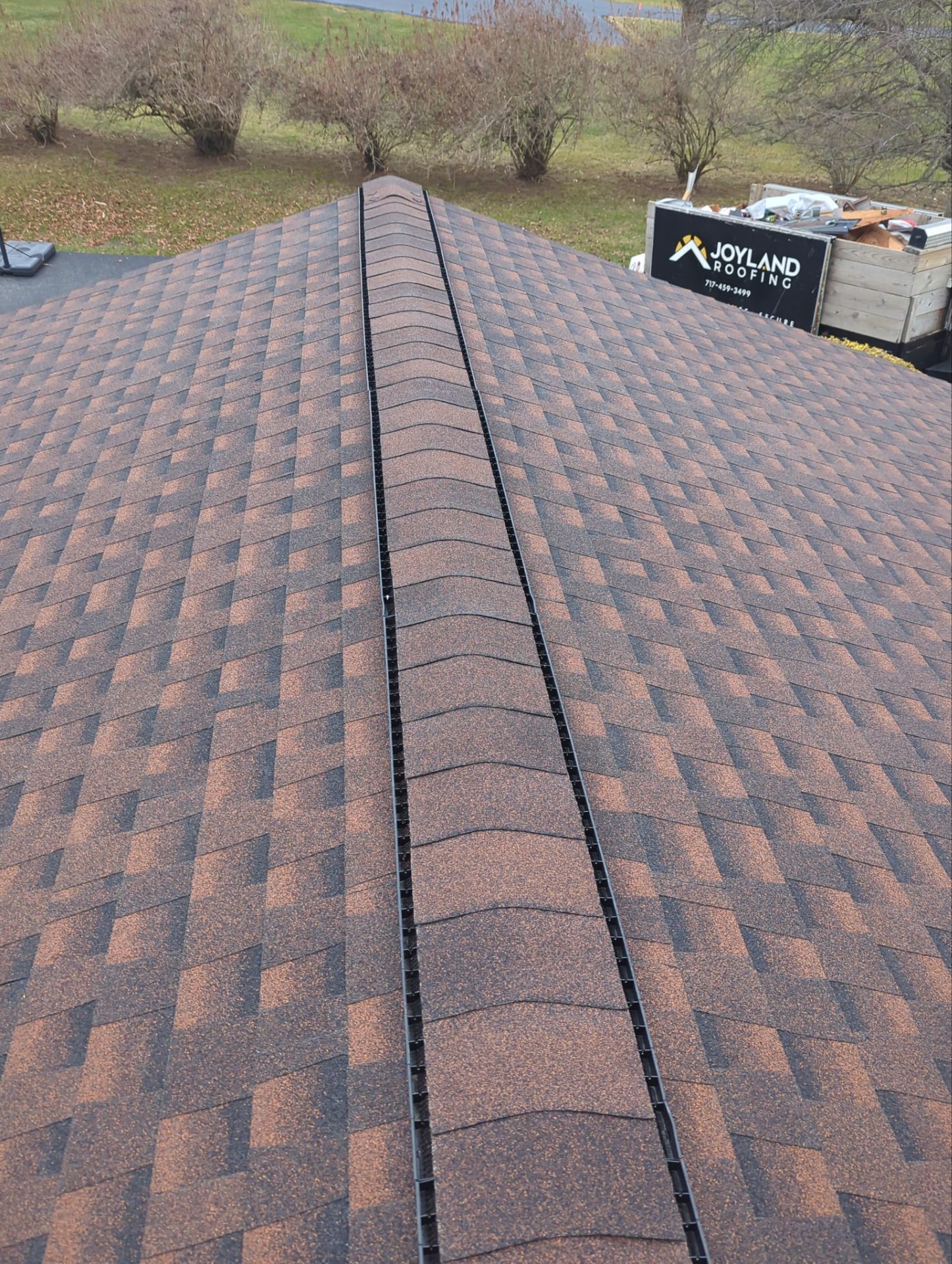 Brown shingled roof with a dark brown ridge.  Overhead view, outdoors.