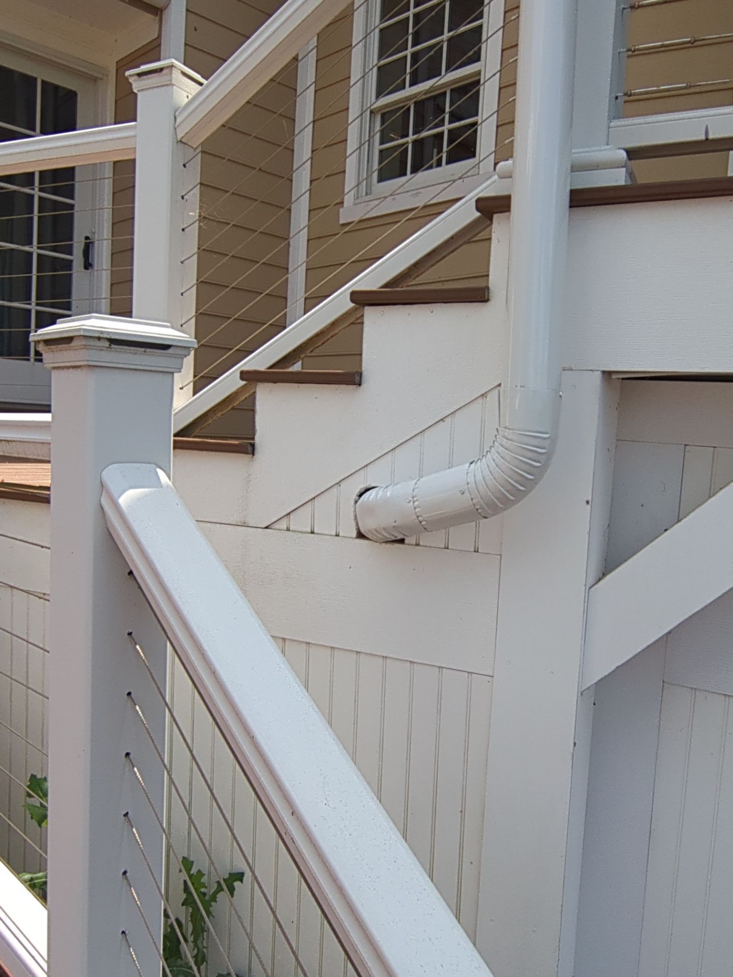 White porch railing with cable infill, steps, and a downspout.