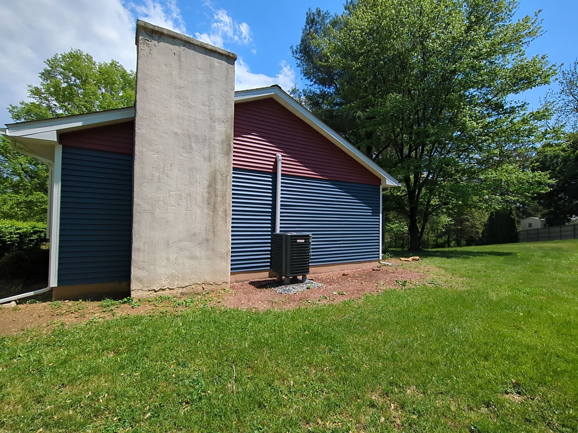 A building with blue and red siding, a concrete chimney, and an HVAC unit on a grassy lawn.
