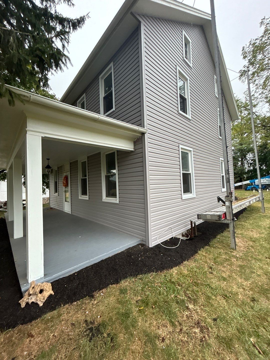 Three-story house with gray siding, white trim, and a porch with dark gray flooring.