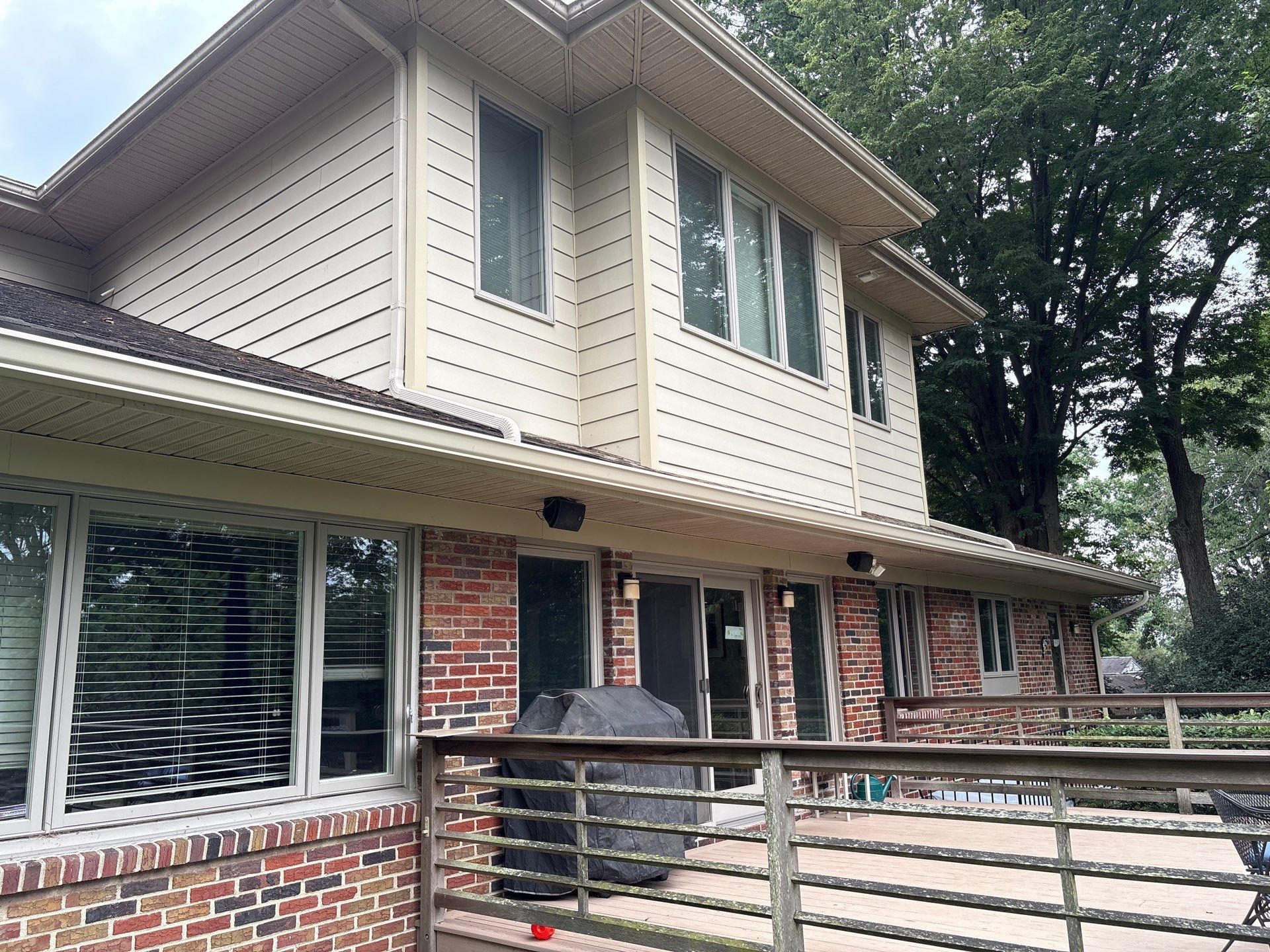 Two-story house with tan siding, brick facade, and a wooden deck.